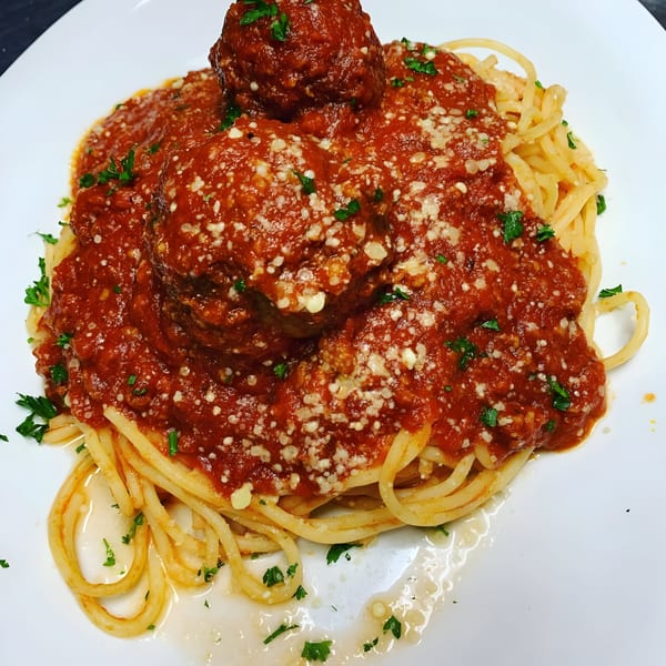 Spaghetti and meatballs with red sauce, parmesan cheese, and parsley on a white plate.