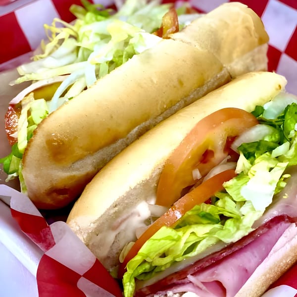 Two Franco's Italian subs with lettuce, tomato, and meat in a red and white checkered basket.